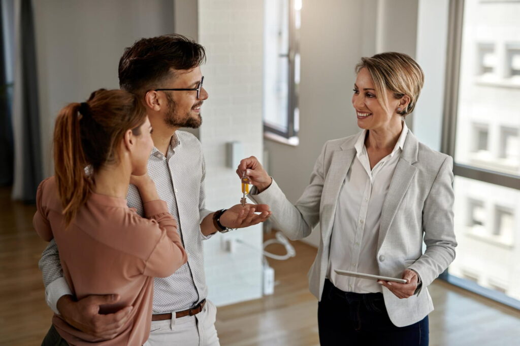 Real estate agent handing house keys to a happy couple, illustrating how AI in real estate streamlines property transactions and enhances the customer experience.