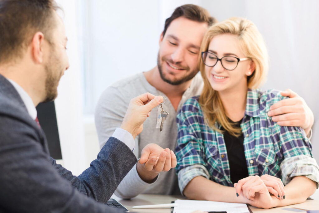 A real estate agent handing over house keys to a smiling couple, representing a successful Sotogrande property purchase and professional property services.